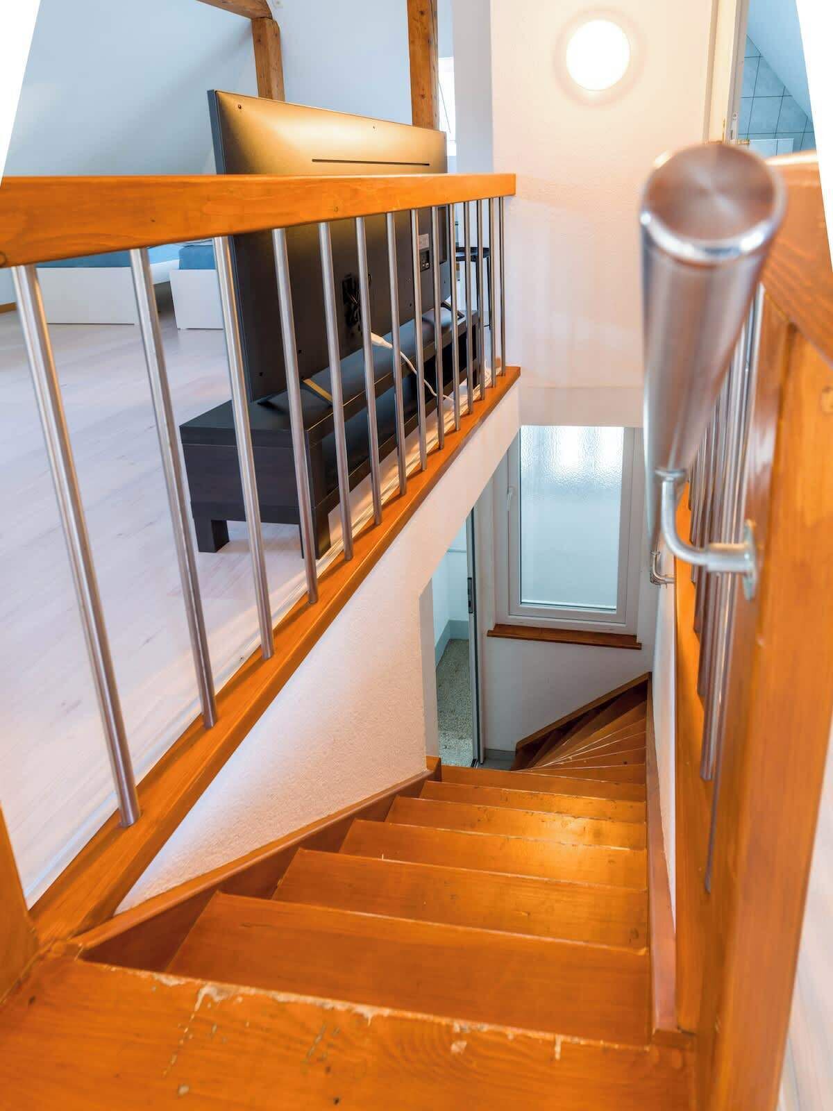 Una escalera de madera con barandilla metálica que conduce a una habitación con cama y ventana.