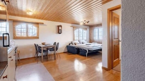 A room with a wooden ceiling, a bed, a dining table with chairs, and a kitchen area. - Alpine Garden Retreat | Panoramic Mountain Views (Reichenbach im Kandertal)