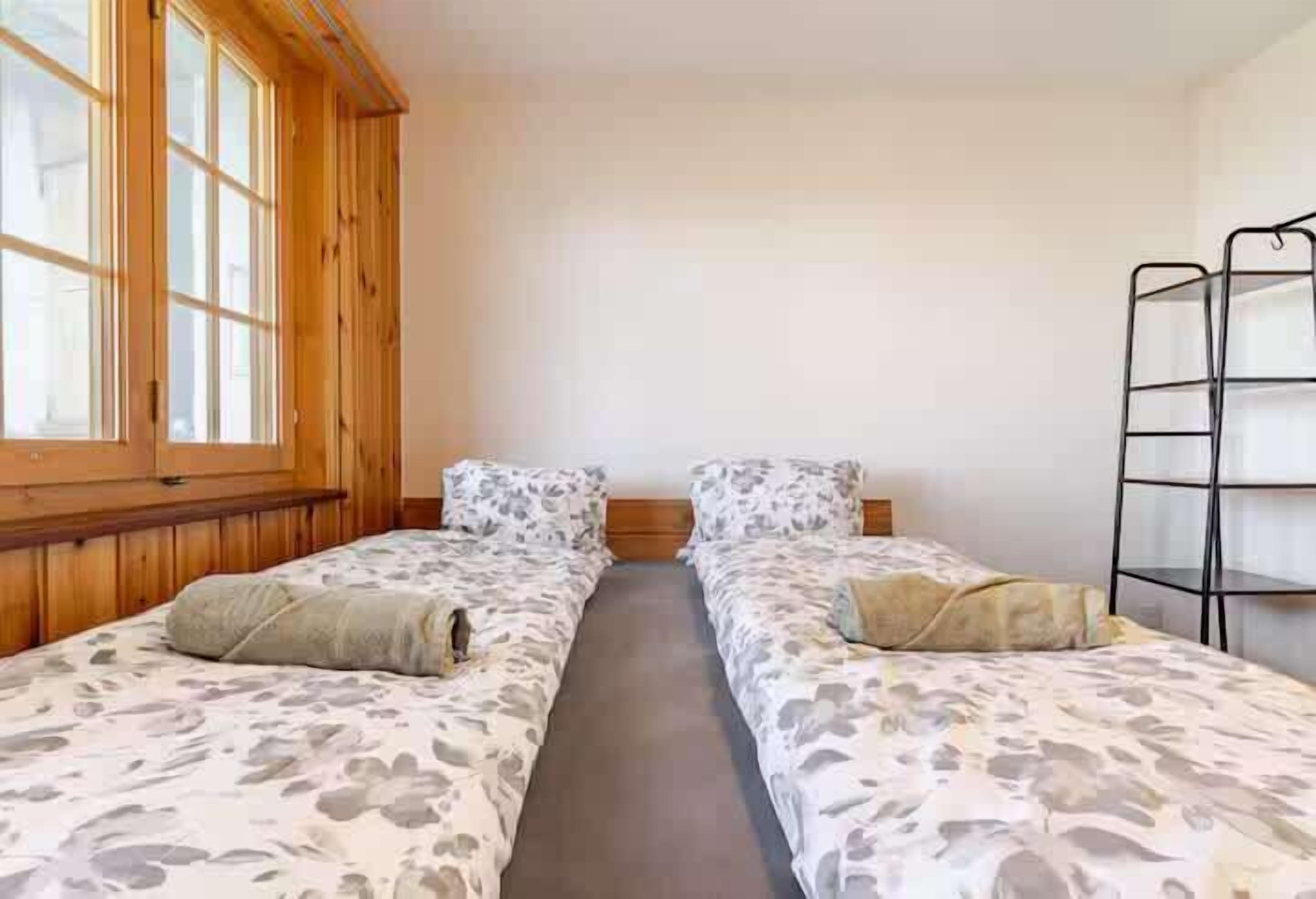 Een kamer met twee bedden, houten wanden, een raam en een metalen plank.