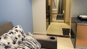 Een hotelkamer met een bank, een tafeltje, een badkamer met douche en een keukenhoek.