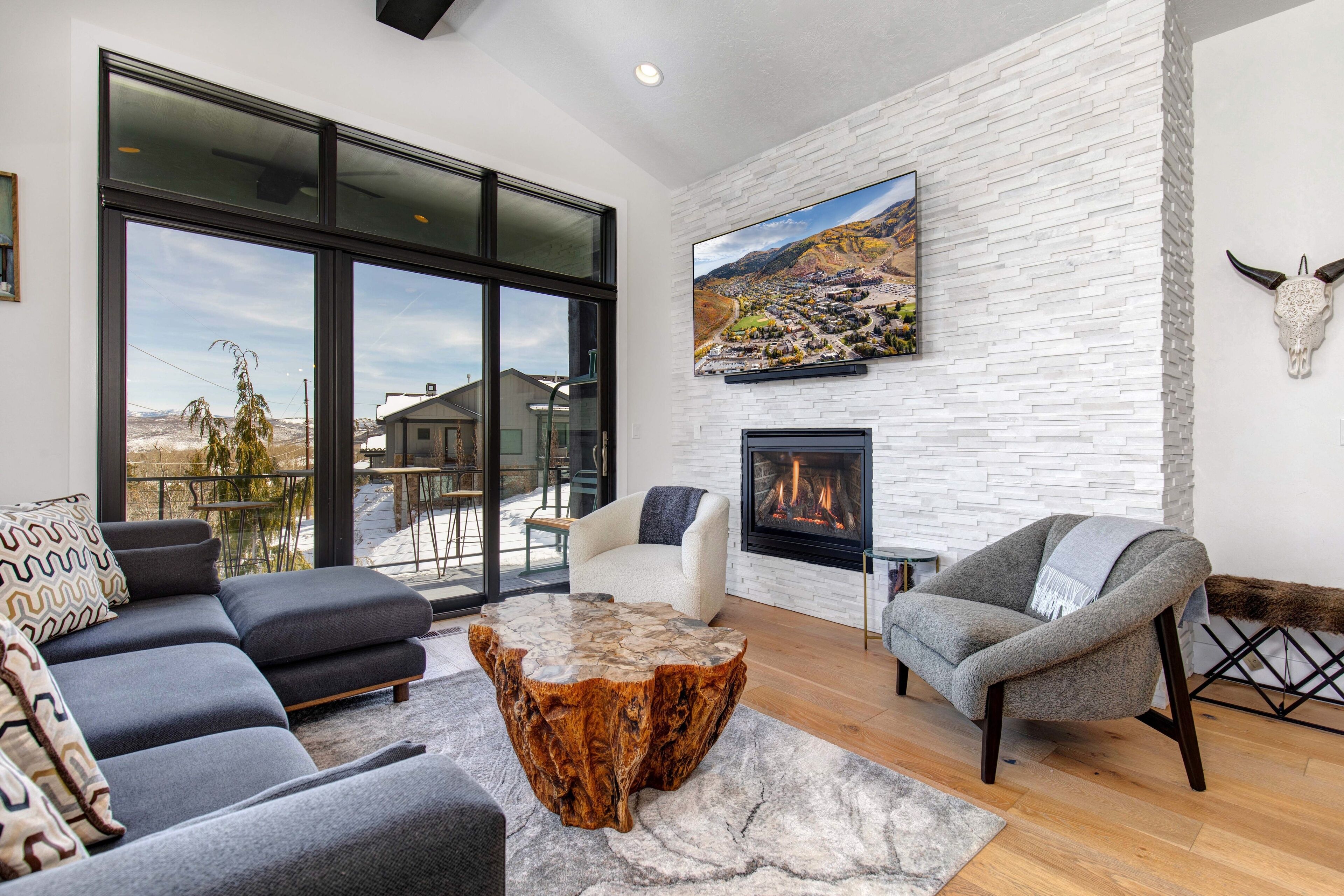 A modern living room with a fireplace, a large window, and a view of the outdoors.