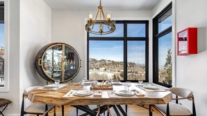 Un comedor con una mesa de madera dispuesta para cuatro, una araña y un ventanal con vistas a un paisaje nevado.