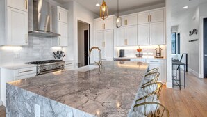 Una cocina moderna con armarios blancos, una isla de mármol y detalles dorados.