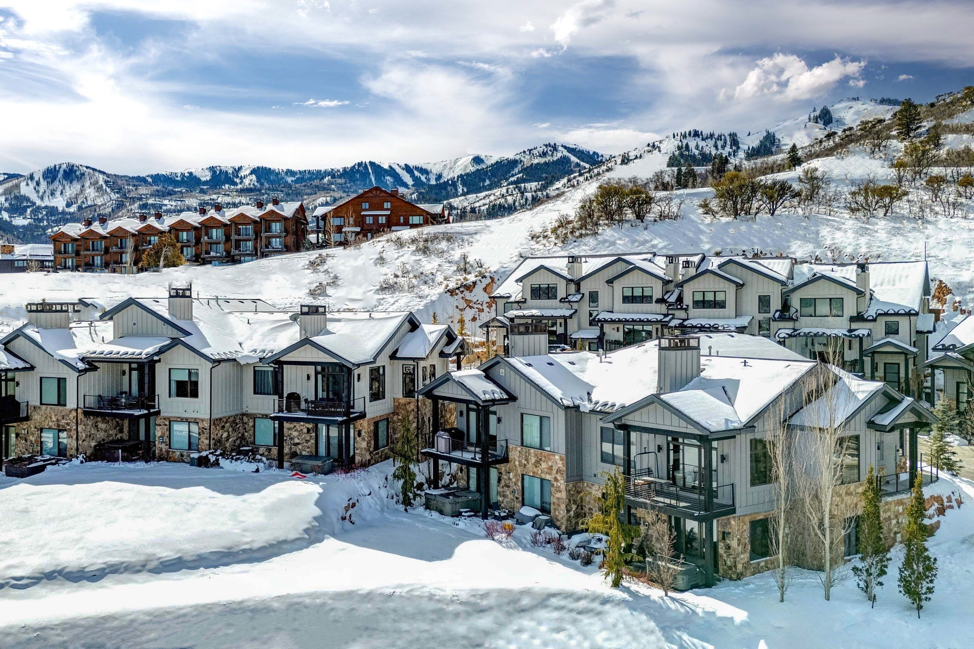 Een besneeuwde badplaats met moderne gebouwen, een skipiste op de achtergrond en bergen.