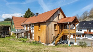 Ein Holzhaus mit rotem Dach, einem Balkon und einer Treppe zum Eingang.