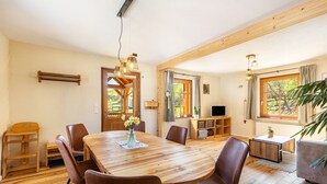 Ein Holzespeisesaal mit Stühlen, einer Blumenvase und einem Fernseher in einem gemütlichen Raum mit Holzböden und großen Fenstern.