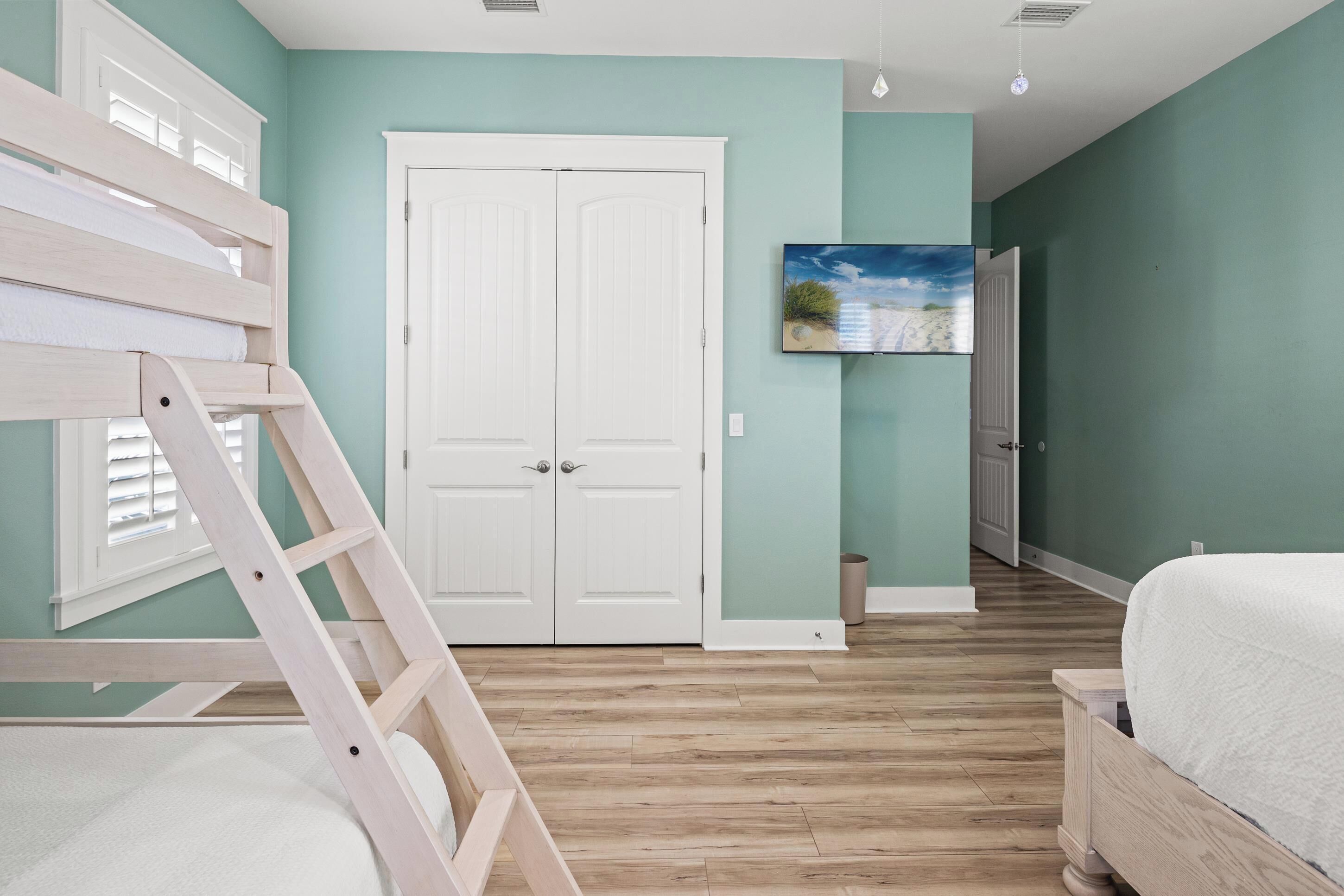 A bedroom with a bunk bed, a white door, a painting on the wall, and a wooden floor.