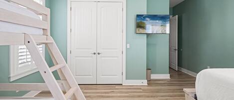 A bedroom with a bunk bed, a white door, a painting on the wall, and a wooden floor.