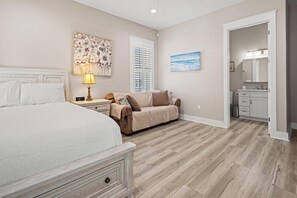 A bedroom with a large bed, a nightstand, a lamp, a beige sofa, and a painting. - Beach House - Magical Purple Haze (Mexico Beach)