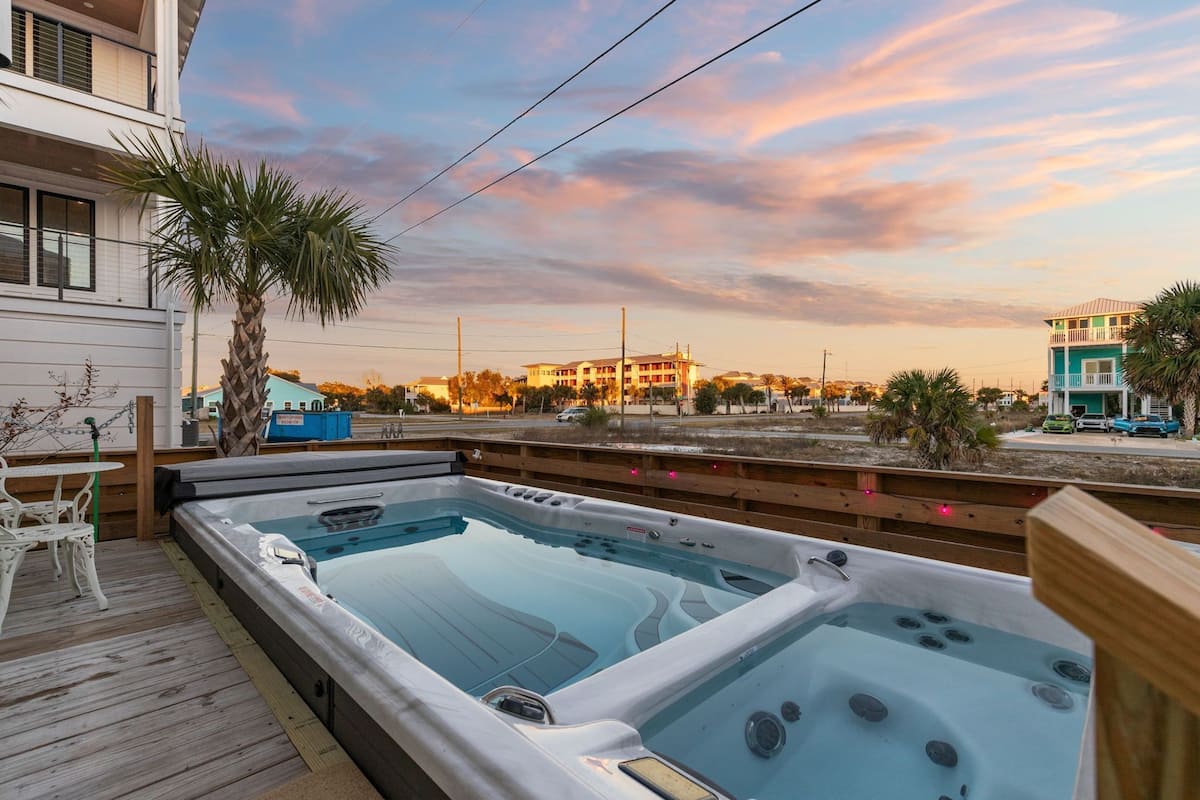 Un área de piscina en la azotea con dos jacuzzis, una terraza de madera y vistas a edificios al fondo.