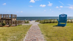 A beach pathway leading to the ocean, a wooden structure, and a blue chair with a sign. - Beach House - Magical Purple Haze (Mexico Beach)
