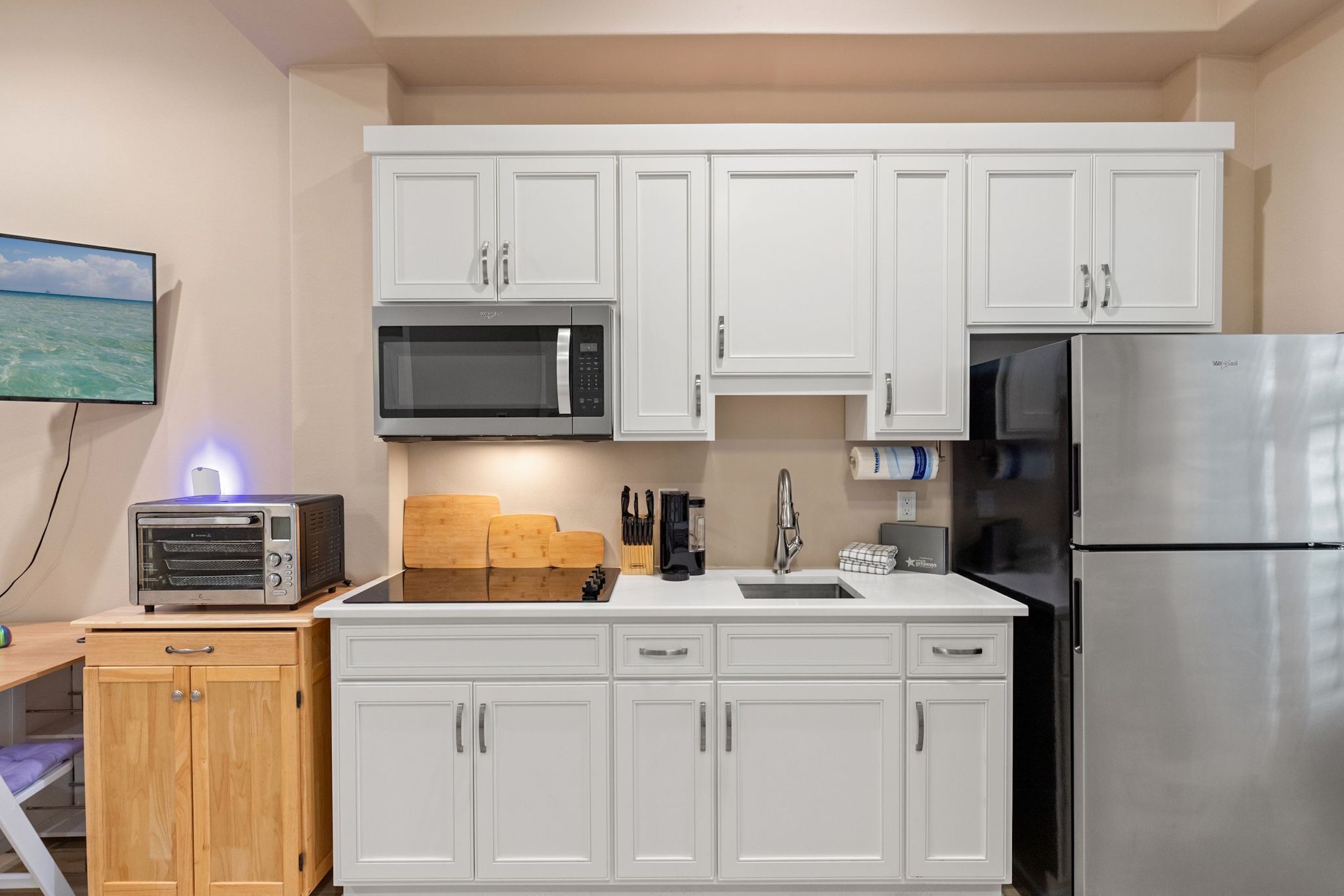 A modern kitchen with white cabinets, a stainless steel refrigerator, a microwave, and a toaster.