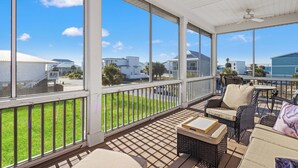 A covered outdoor patio with wicker furniture, large windows, and a view of a residential area. - Beach House - Magical Purple Haze (Mexico Beach)