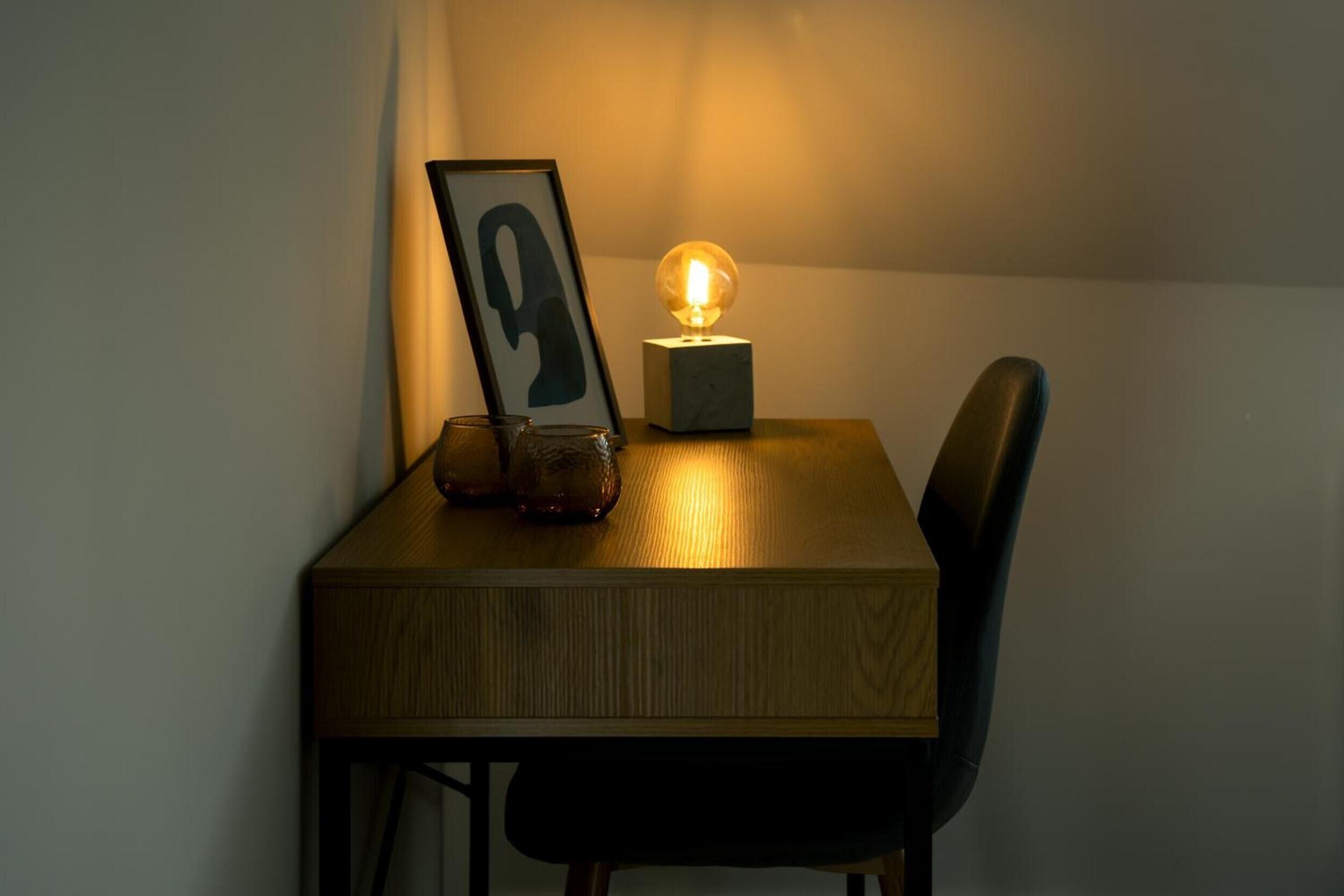 A wooden table with a framed picture, a glass, and a spherical light fixture.