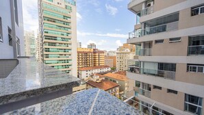A high-rise building with multiple balconies, a mix of residential and commercial structures, and a clear sky.