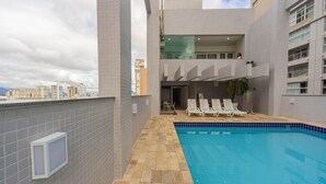 A rooftop swimming pool with lounge chairs, a tiled floor, and a city view.