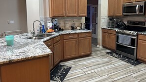 Una cocina con armarios de madera, encimera de granito, pileta de acero inoxidable y microondas.