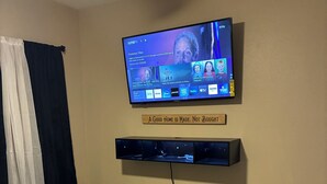 Un dormitorio con una cama, un televisor montado en la pared y una estantería debajo.