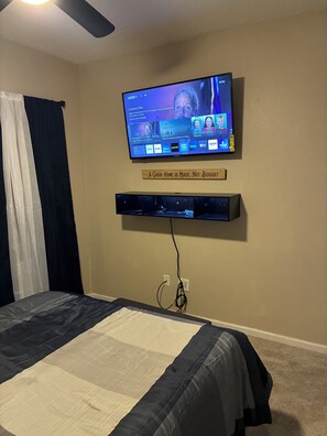 Ein Schlafzimmer mit einem Bett, einem an der Wand befestigten Fernseher und einem darunterliegenden Regal.