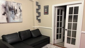 Una sala de estar con un sofá de cuero negro, una puerta con marco blanco y un cuadro abstracto gris en la pared.