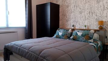 Ein Schlafzimmer mit Bett, Kleiderschrank, Fenster und einer Wand mit Blätermotiv.