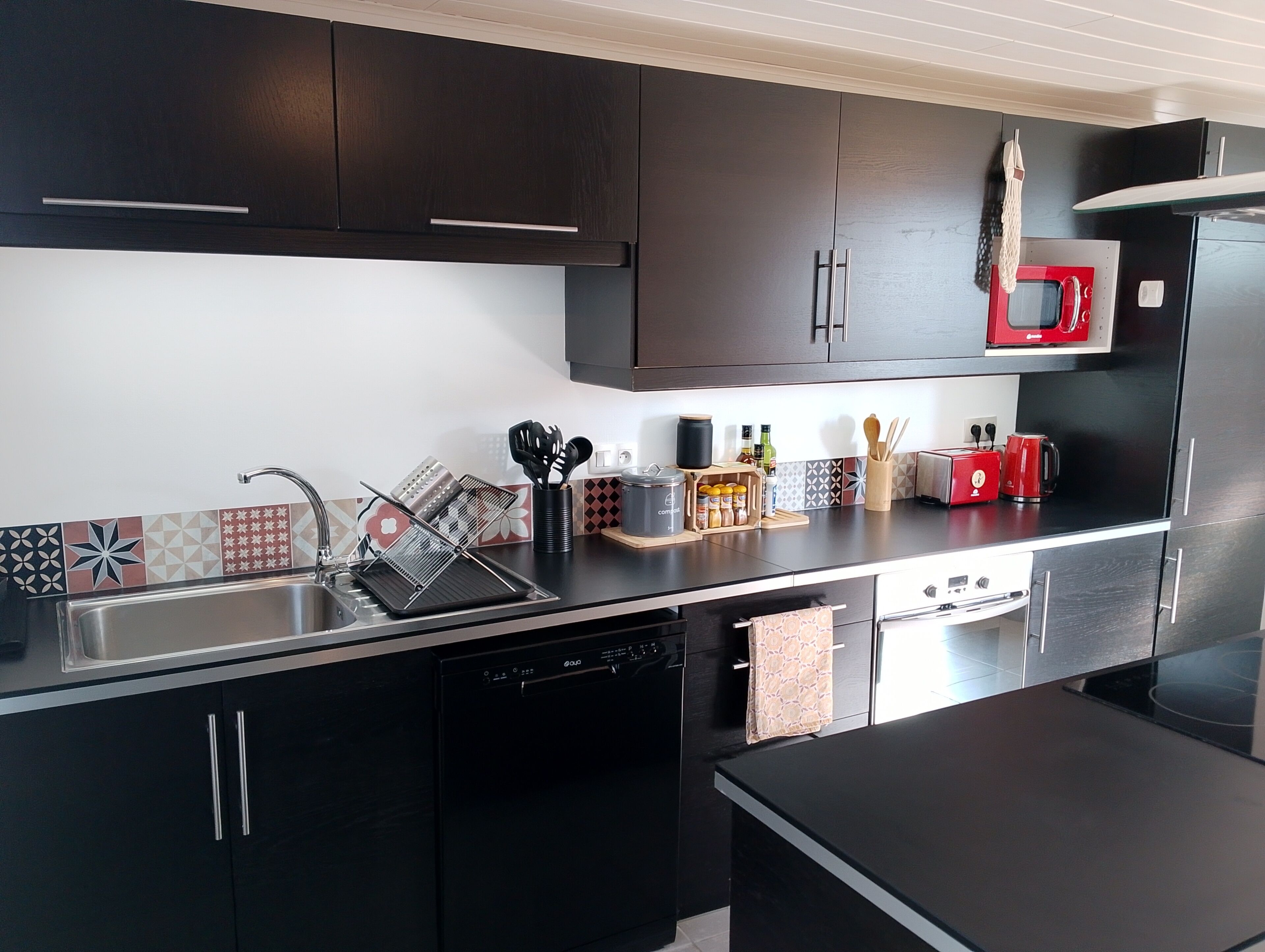 Une cuisine moderne avec des meubles de couleur sombre, un évier en acier inoxydable et un grille-pain rouge.