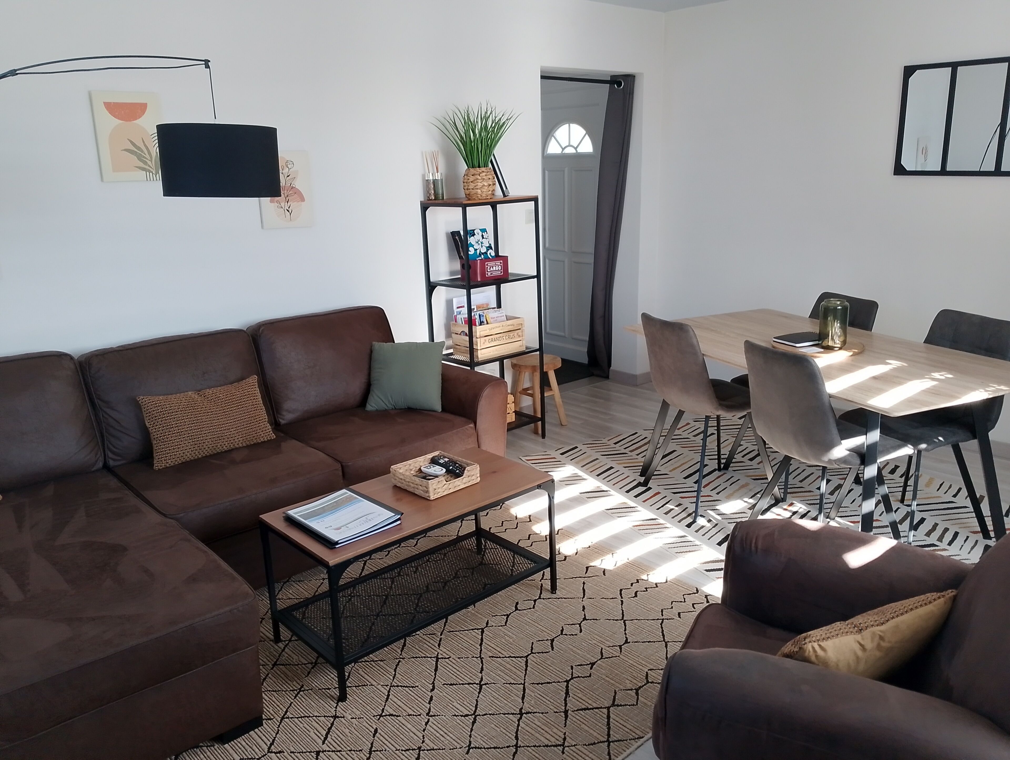 A living room with a brown sofa, a coffee table, a bookshelf, and a dining area with a table and chairs.