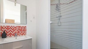 A bathroom with a white sink, red and white tiled backsplash, and a shower with horizontal lines. - Le Sarrail - Hypercentre & sleeps 12 (Reims)
