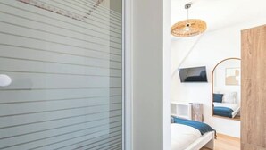 A bedroom with a bed, a TV, a mirror, and a wooden wardrobe. - Le Sarrail - Hypercentre & sleeps 12 (Reims)