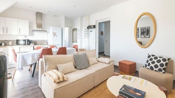 A modern living room with a sofa, coffee table, and a dining area with chairs and a table. - Le Sarrail - Hypercentre & sleeps 12 (Reims)