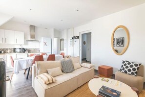 A modern living room with a sofa, coffee table, and a dining area with chairs and a table. - Le Sarrail - Hypercentre & sleeps 12 (Reims)