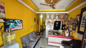 Una zona de recepción con televisor, asientos, dispensador de agua y mostrador con objetos religiosos.