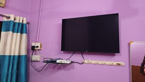 Una habitación con paredes moradas, un televisor negro montado en la pared, una regleta de enchufes y una cortina de ducha a rayas azules y blancas.