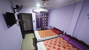 Una habitación con dos camas, ventilador de techo, aire acondicionado y televisor montado en la pared.