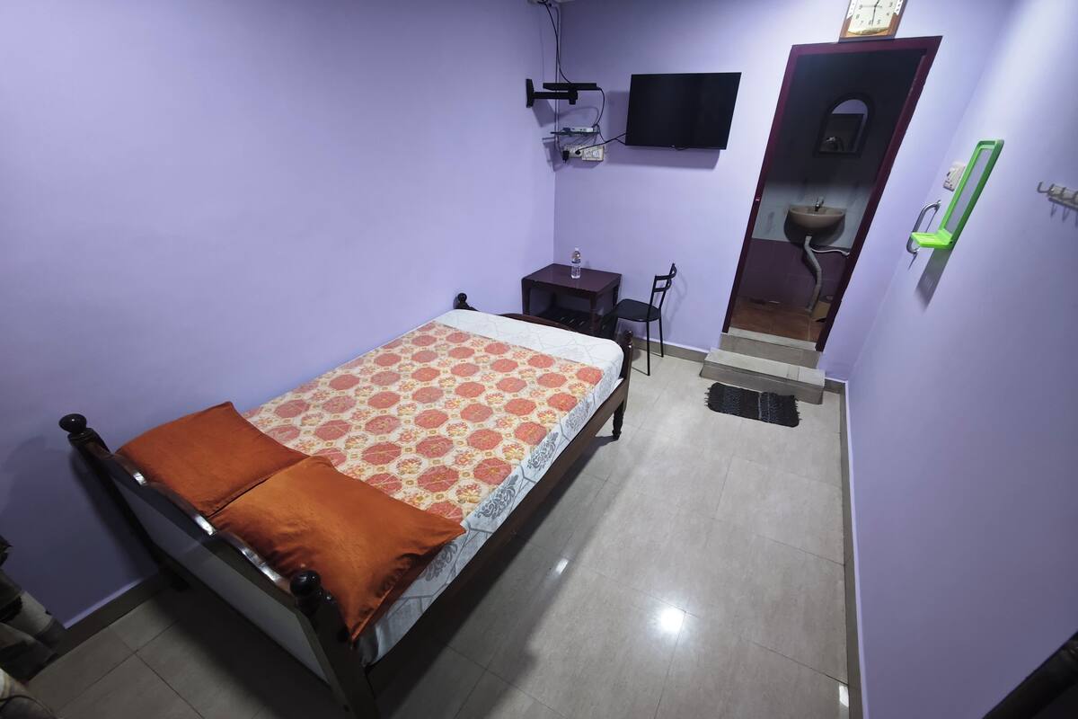 A bedroom with a bed, a chair, a TV, a mirror, and a small table.