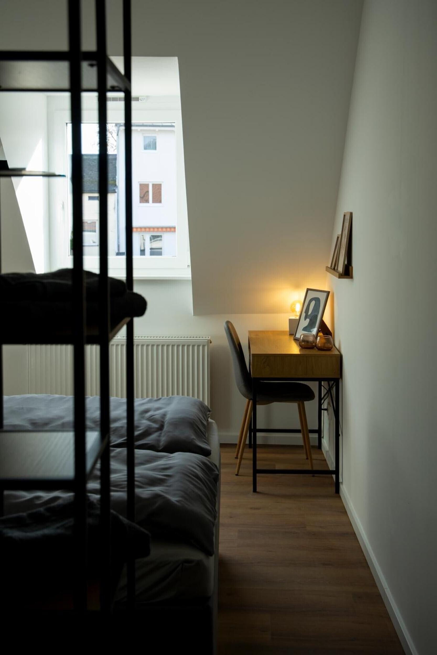 Un dormitorio con una cama litera, un escritorio con silla, un ventanal pequeño y un radiador.