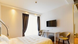 A hotel room with a bed, desk, chairs, and a TV. - Studio by Alliance (Batumi)