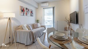 Un salon moderne avec un canapé, une table à manger dressée avec des assiettes et des verres, un lampadaire et des œuvres d’art accrochées au mur.