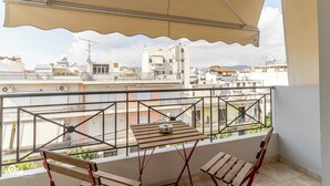 Un balcon avec une table et des chaises en bois, un auvent beige et une vue sur les bâtiments environnants.