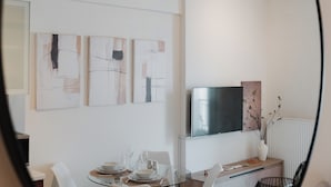 Un espace de restauration moderne avec une table en verre, des chaises blanches et des œuvres d’art abstraites accrochées au mur.