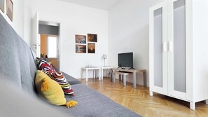 A modern living room with a grey sofa, a TV, a small white table, and a cabinet. - Bright Apartment with Balcony | Workspace (Wrocław)