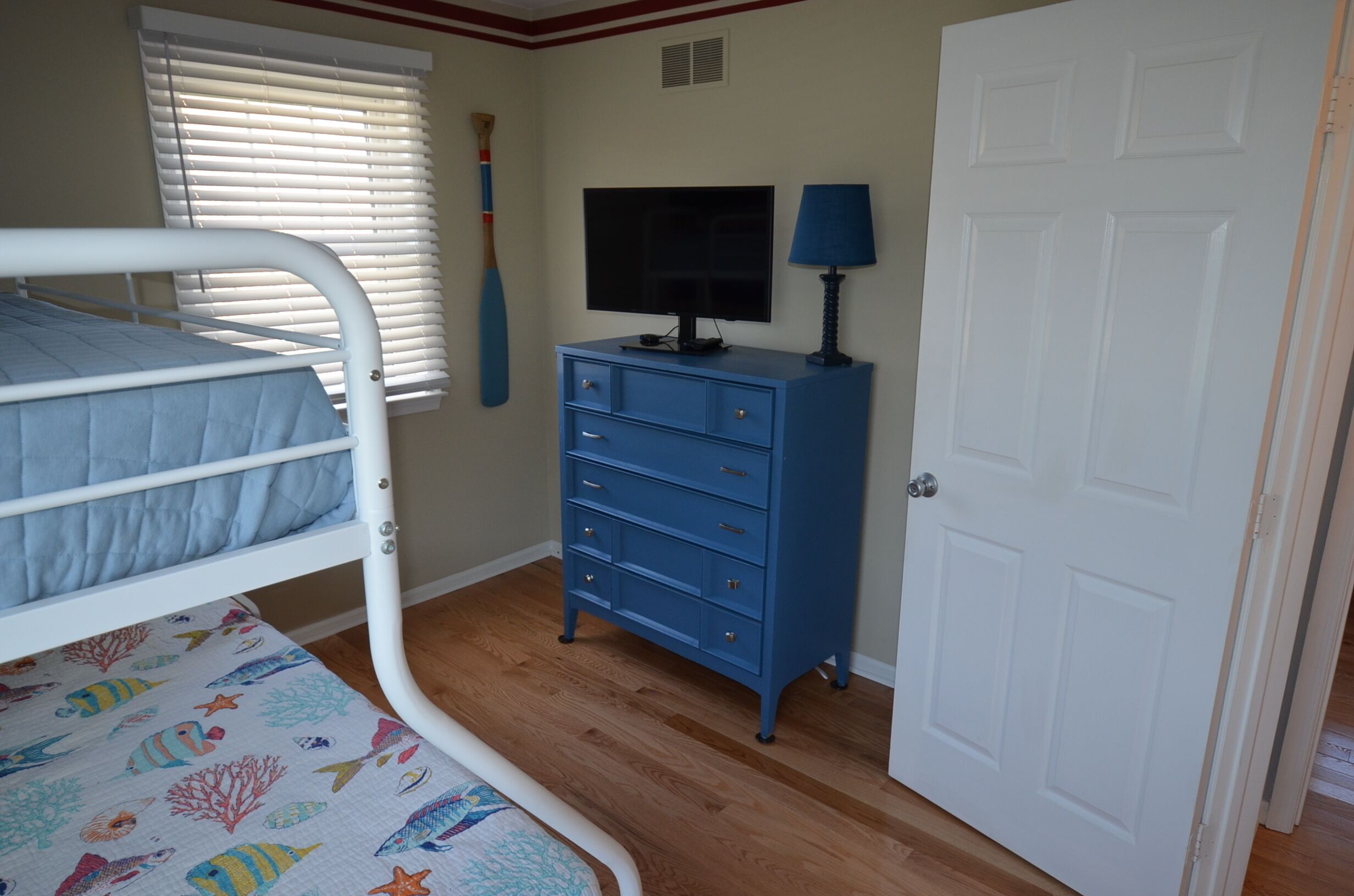 Een slaapkamer met een stapelbed, een dressoir, een televisie en een deur.