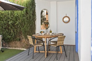 Uma mesa de madeira redonda com quatro cadeiras de vime, um espelho e uma garrafa no convés.