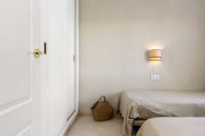 Quarto com cama, luminária na parede, porta e cesta de palha.