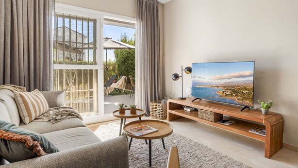 Ein Wohnzimmer mit einer Couch, einem Couchtisch, einem Fernseher und Blick auf eine Küstenlandschaft.