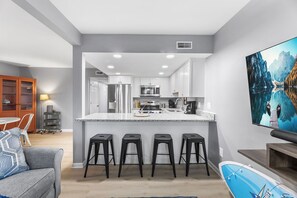 Une cuisine moderne avec des meubles blancs, un grand îlot central doté de tabourets, et un coin repas avec une table et des chaises.
