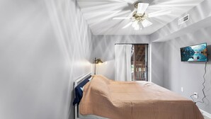 Et soveværelse med seng, ventilator, fjernsyn og et vindue med gardiner.