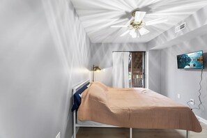 Ein Schlafzimmer mit Bett, Deckenventilator, Fernseher und Fenster mit Vorhängen.