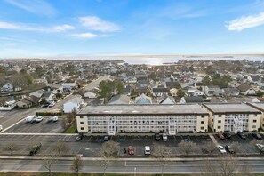 Ein großes Gebäude mit Parkplatz davor, umgeben von Wohnhäusern und einem Gewässer im Hintergrund.