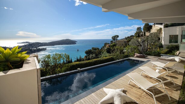 Un espace aménagé au bord de la piscine, avec vue sur la mer, comprenant des chaises longues et un pot de fleurs.